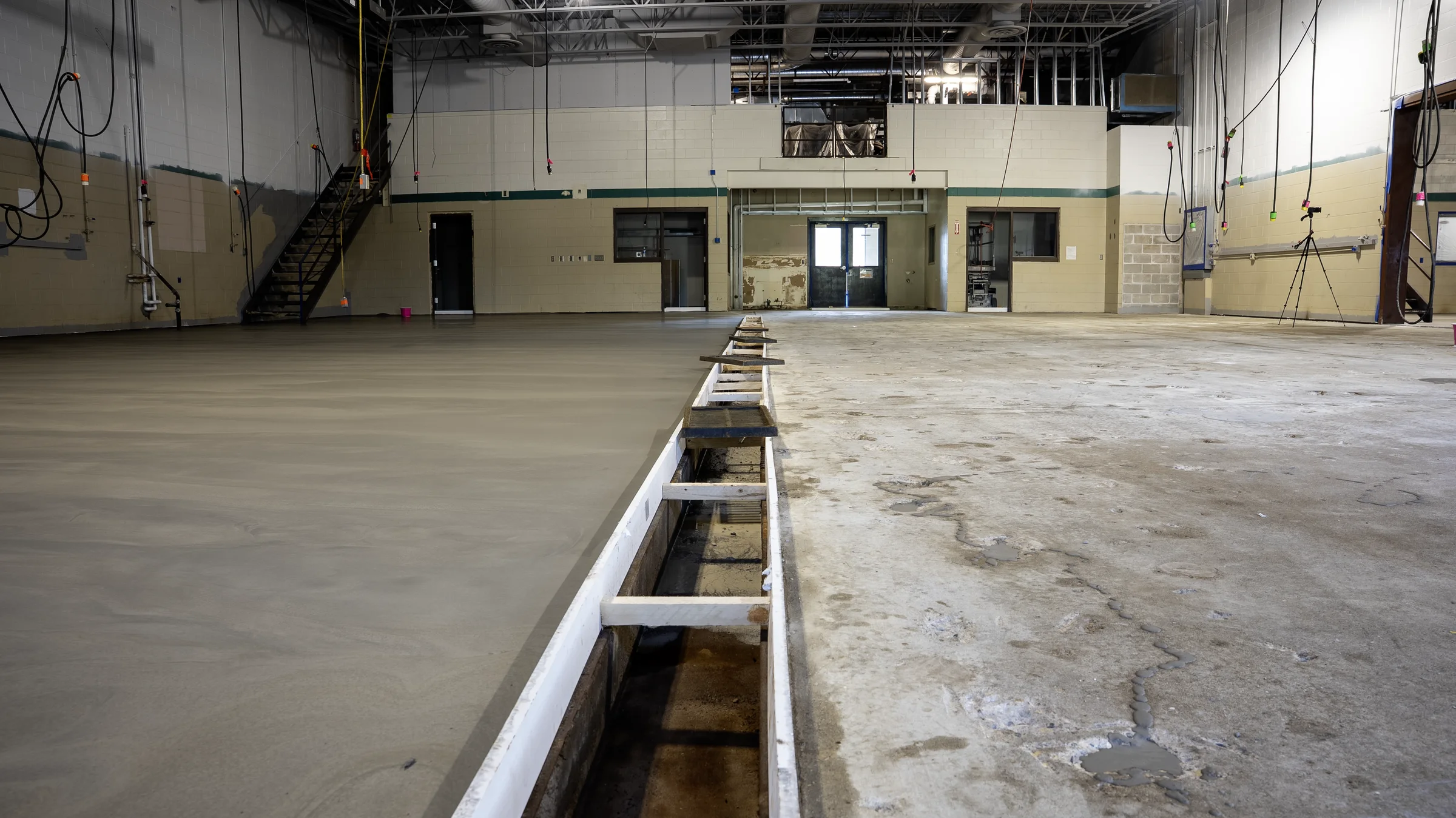 Damaged bare concrete beside a freshly poured self-leveling underlayment section, split by a wood form