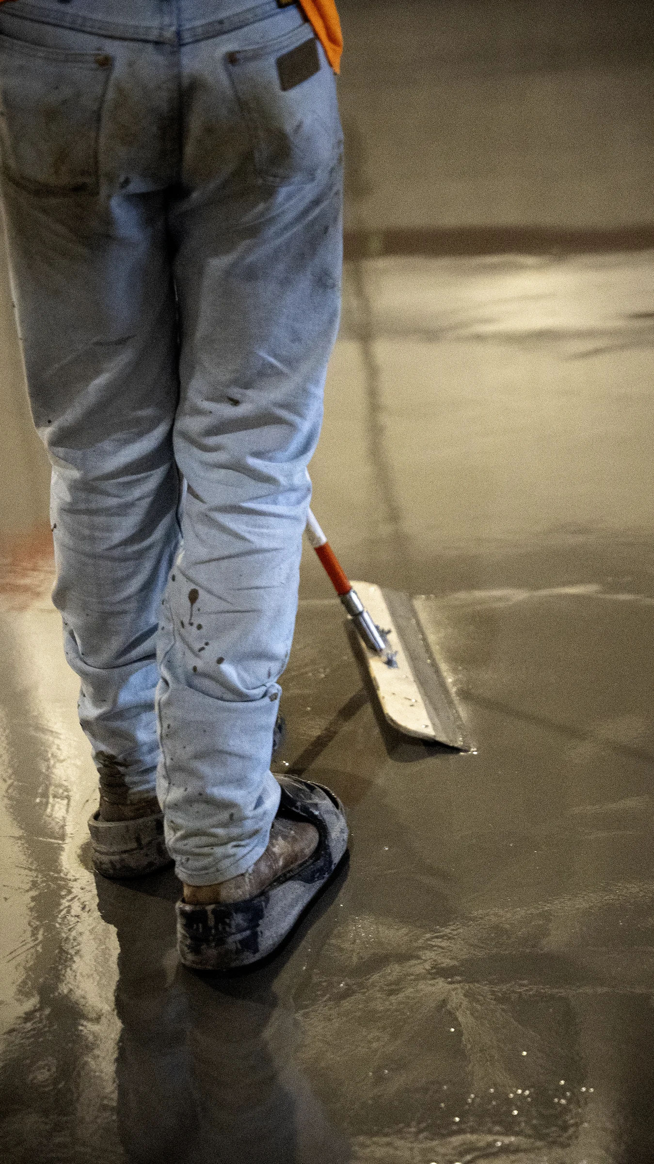 Worker in spiked shoes smoothing wet self-leveling underlayment with a hand tool